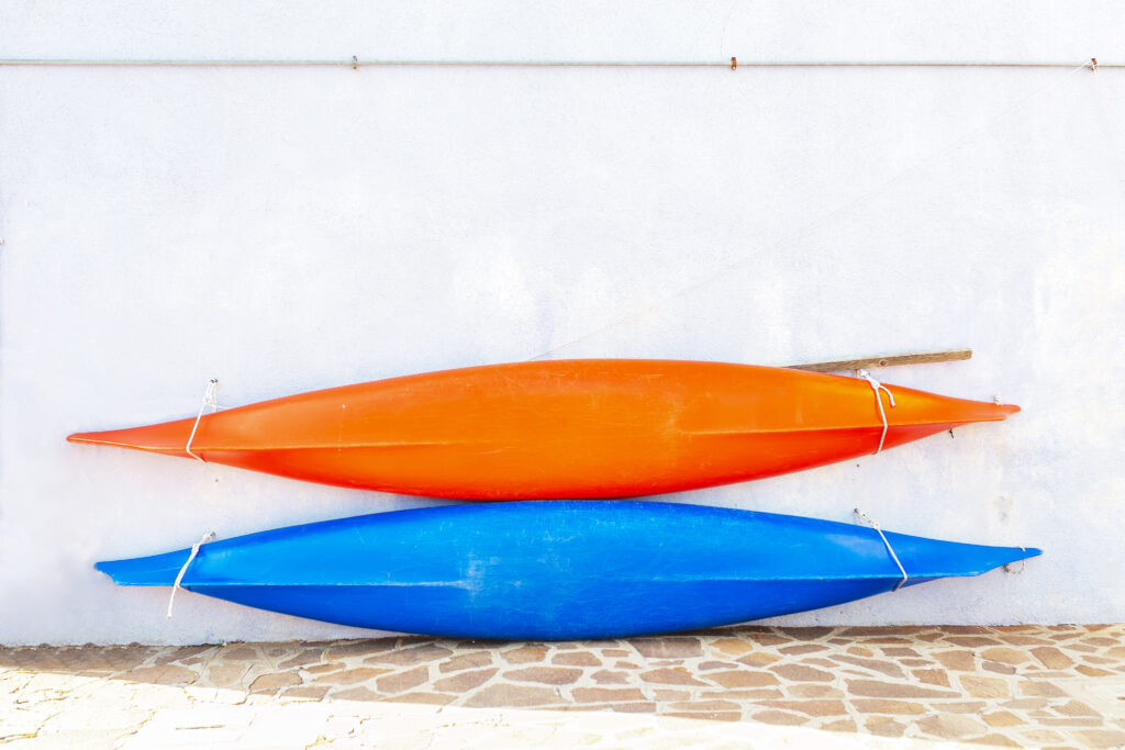 Two kayaks laying up against a wall. One is orange and the other one is blue. 