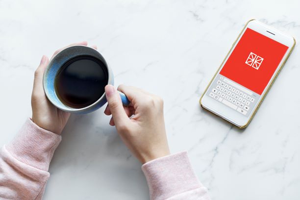 Two hands holding a cup of coffee and a phone showing the Flexistore logo. 