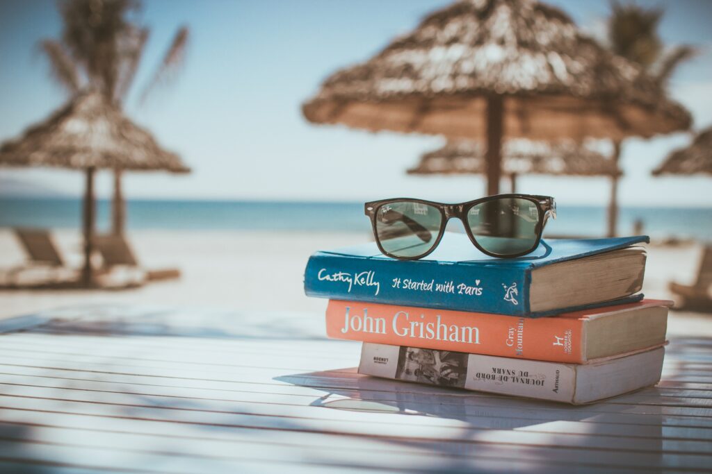 A pair of sun glasses laying on top of three books on a beach. 